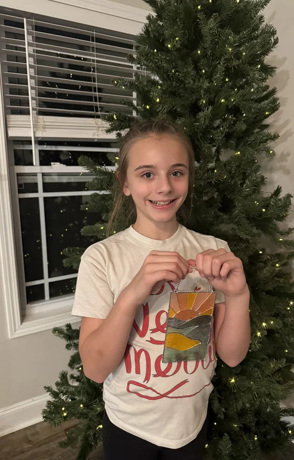 Girl holding her sunset suncatcher in front of a Christmas tree