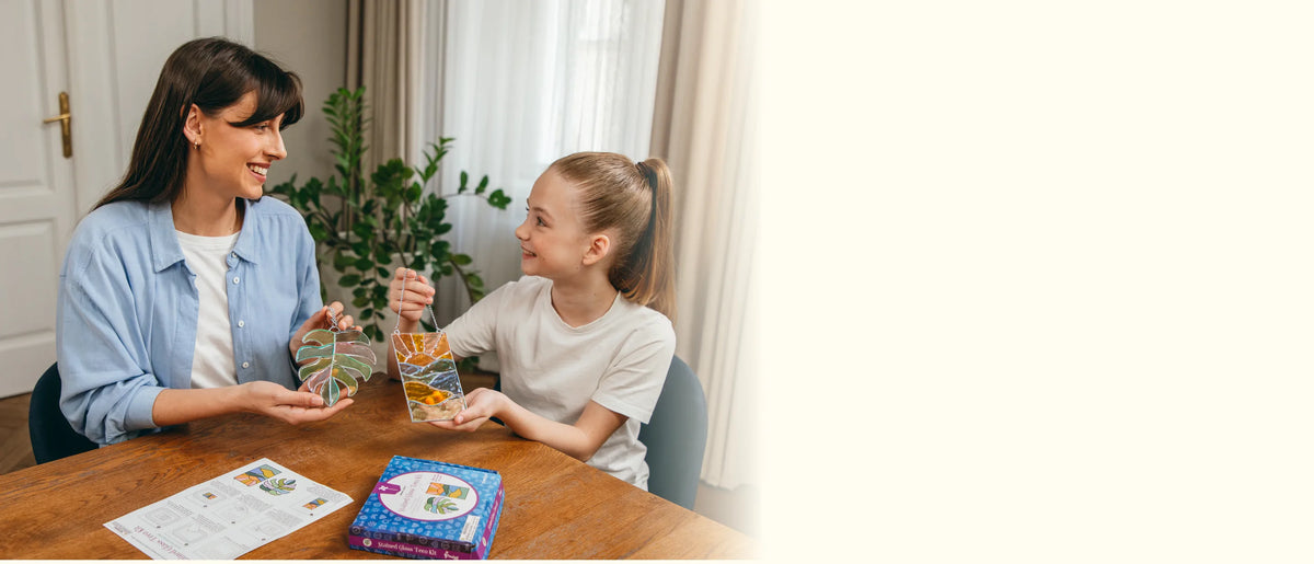 Mother and daughter holding up the finished leaf and sunset suncatchers at the table