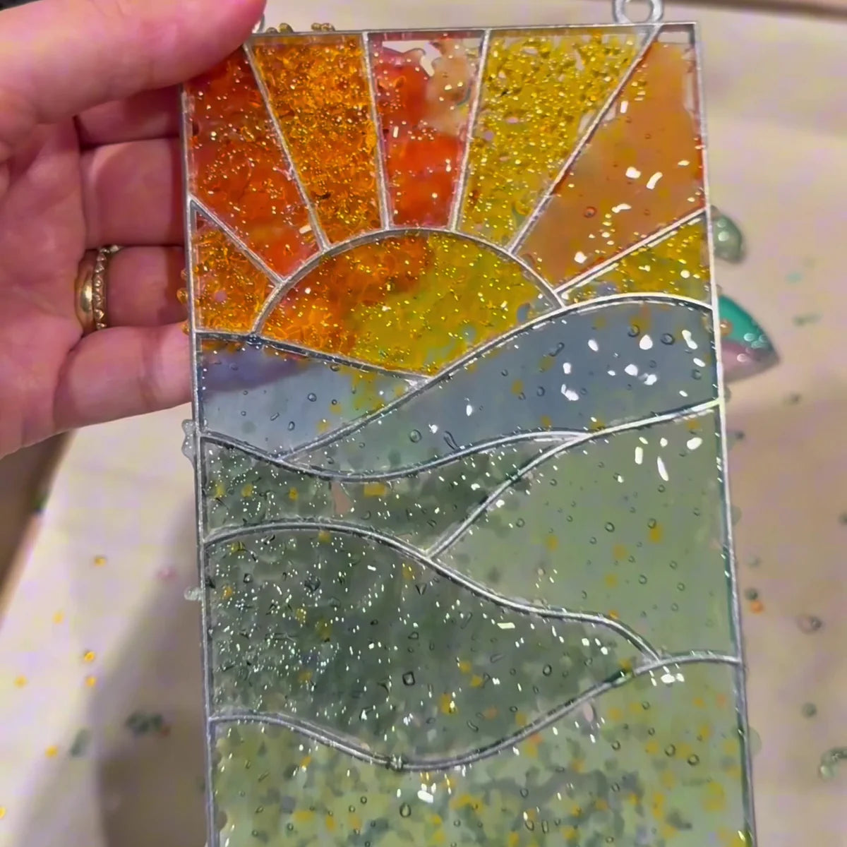 Hand holding the finished sunset suncatcher over the baking tray