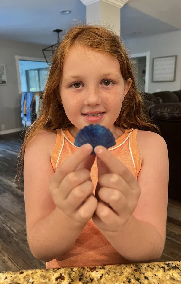 Girl holding a blue glitter shell soap she made in both hands