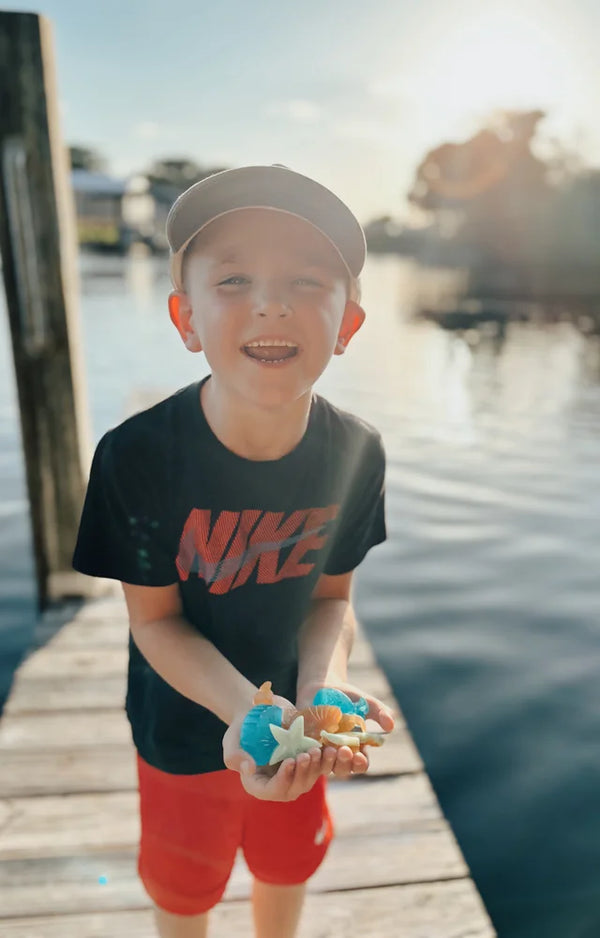 Smiling boy on a dock holding a handful of homemade sea life soaps