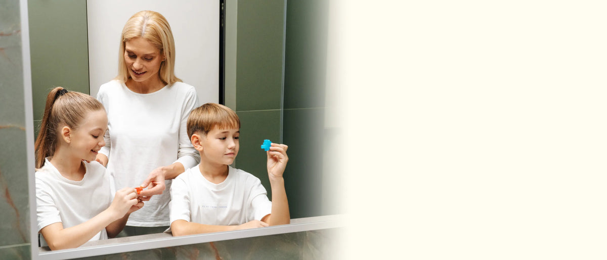 Mom and two kids smiling at the bathroom mirror, holding up the colorful soaps they made