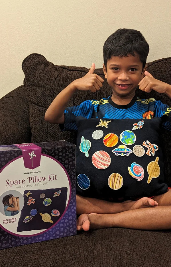 A boy gives two thumbs up behind his finished space pillow, with the kit box beside him