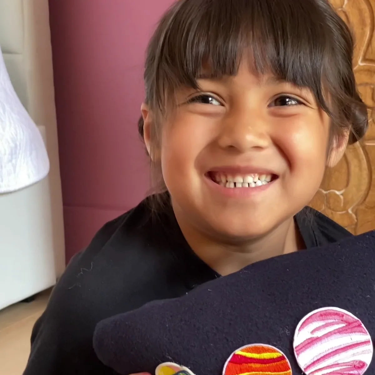A girl smiles as she holds up the finished space pillow she sewed shut and decorated with patches