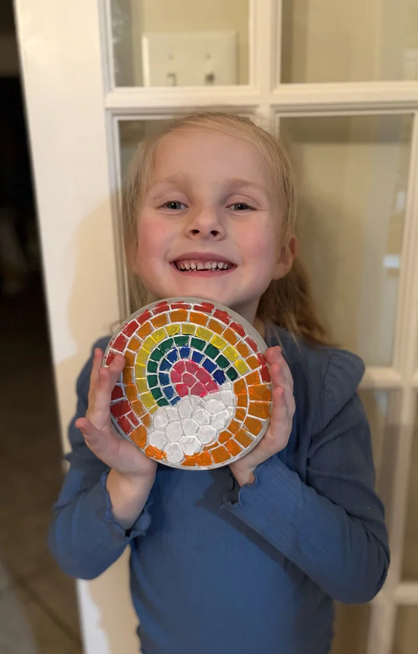Girl smiling with the rainbow mosaic stepping stone she painted