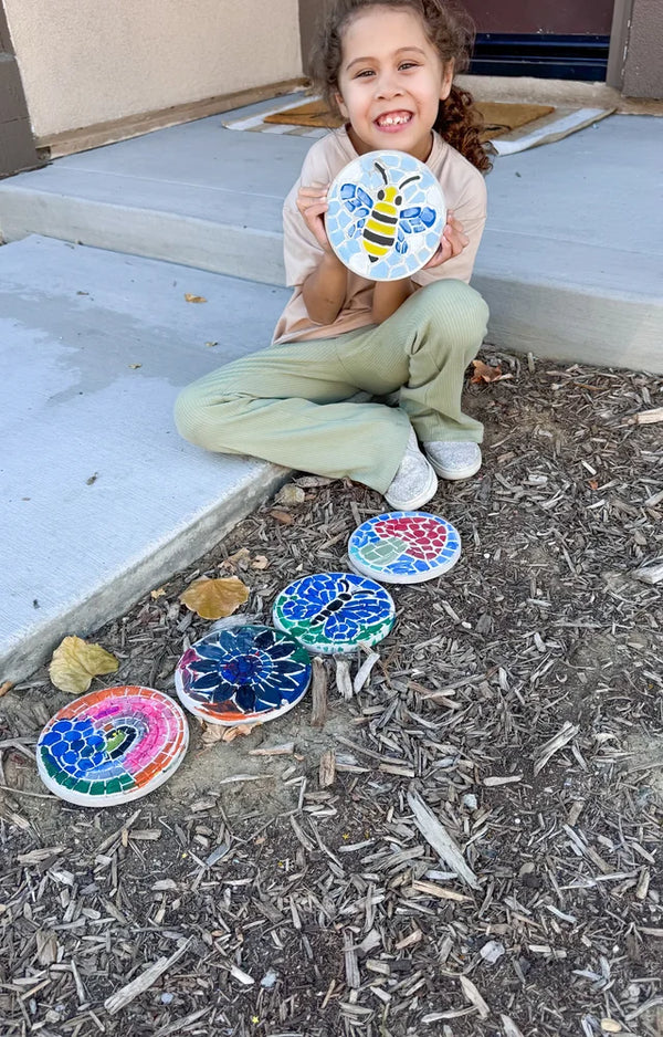 Girl on porch steps holding a painted bee stone, four more stones in the garden mulch