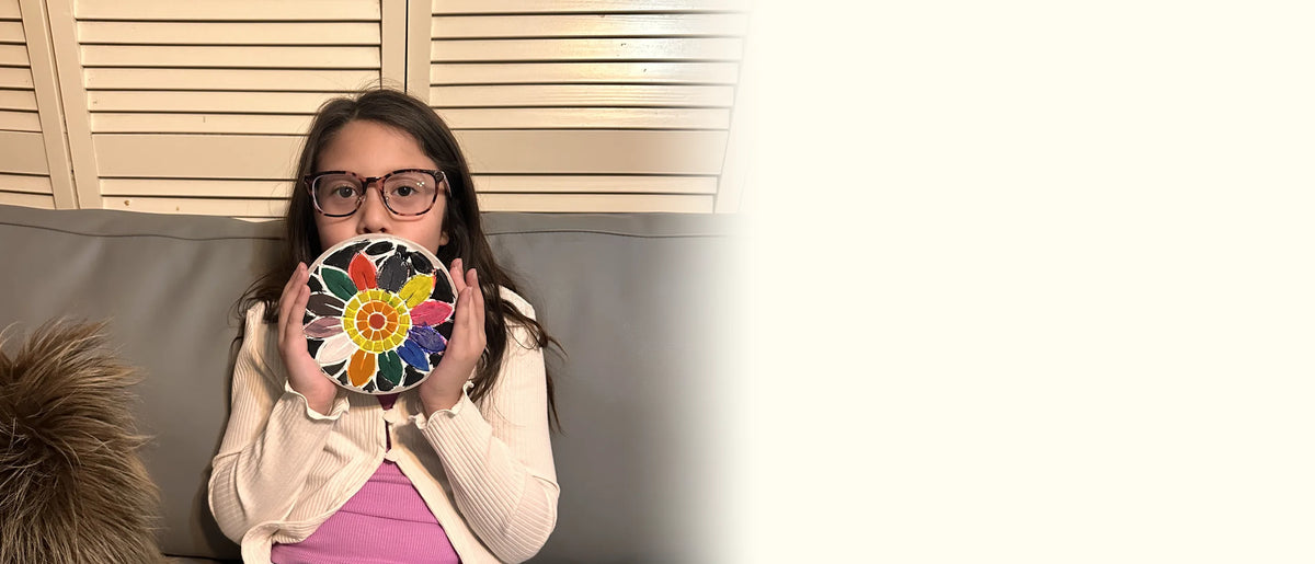 Girl on a sofa holding up her finished painted sunflower mosaic stepping stone