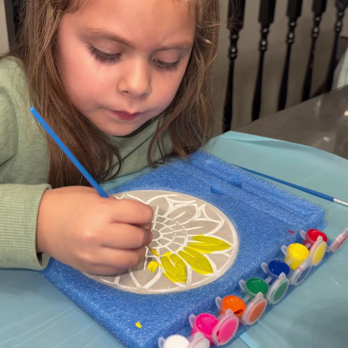 Girl painting the sunflower mosaic stepping stone, her face in view