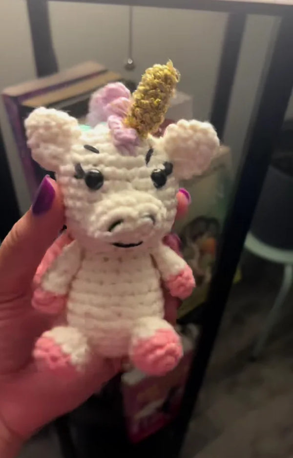 The finished crocheted shimmer unicorn held up in one hand, showing the gold horn and lashes