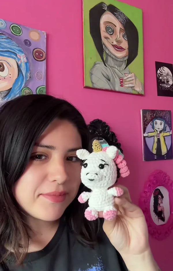 A crafter with her finished crocheted shimmer unicorn standing in front of a pink wall