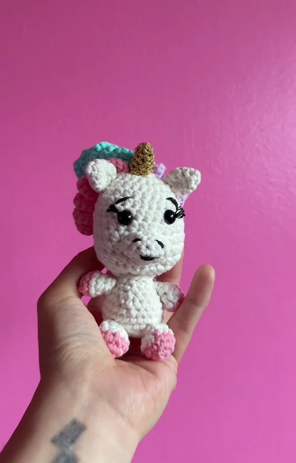 The finished crocheted shimmer unicorn sitting in an open palm against a pink wall