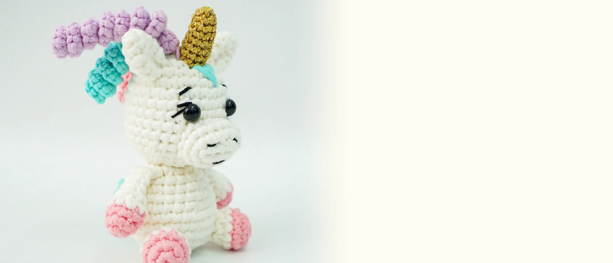The finished crocheted shimmer unicorn with a gold horn and pastel curls on a pale gray background