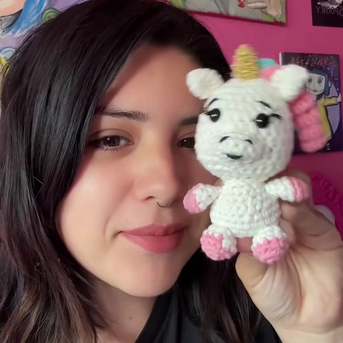 A crafter holds her finished crocheted shimmer unicorn with a gold horn beside her face