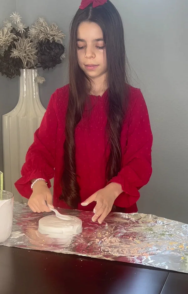 Girl in a red dress smoothing the poured plaster in the round mold on a sheet of foil