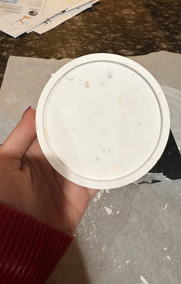 A hand holding the finished trinket dish up close, its small colorful speckles visible in the plaster