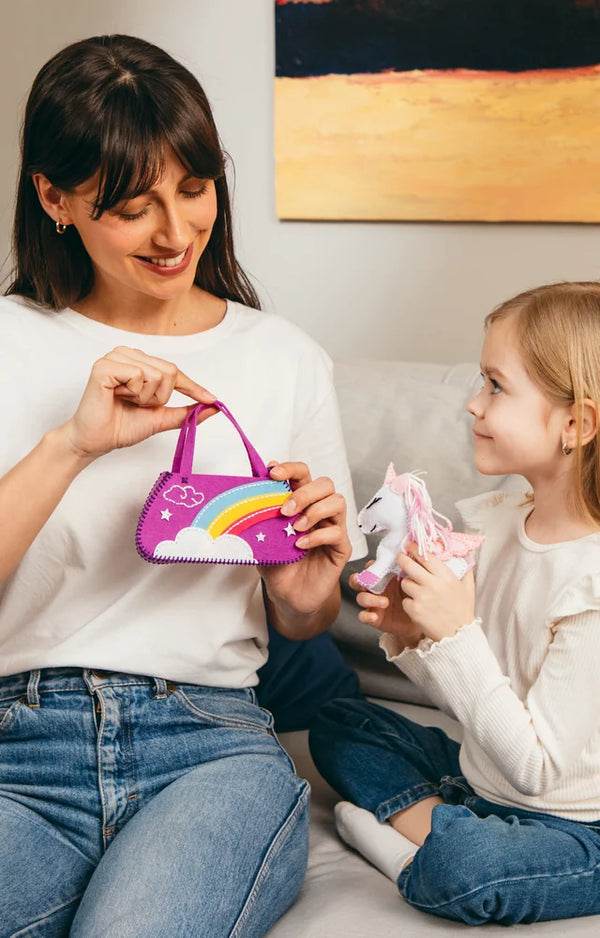 A mother holds up the finished felt rainbow purse while her daughter holds the plush unicorn