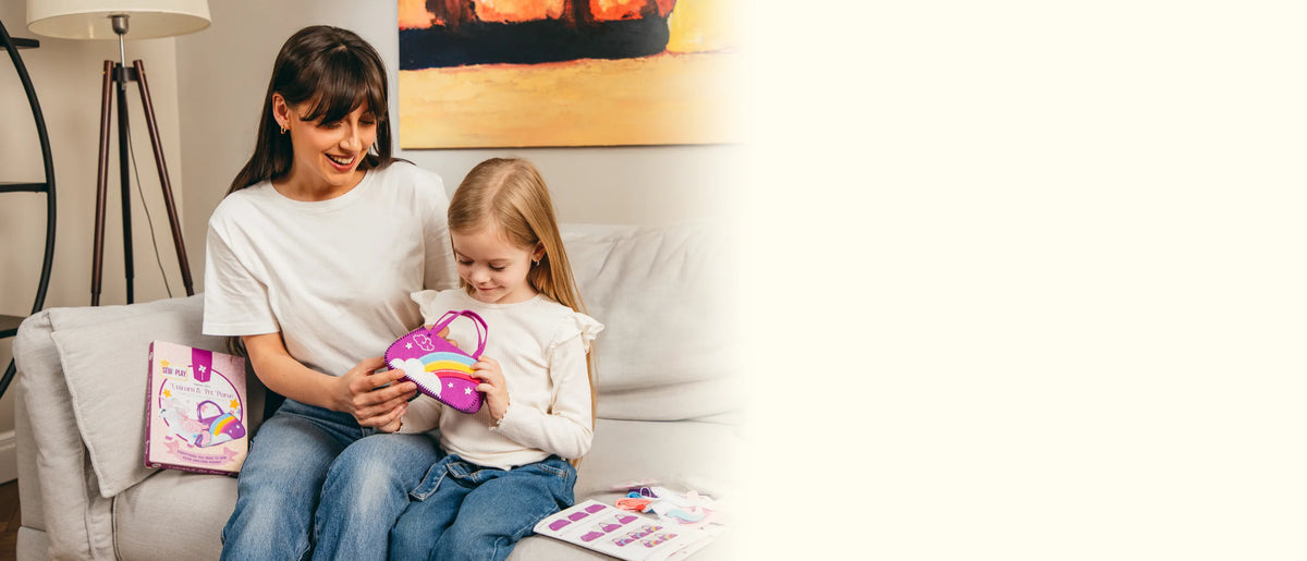 A mother and daughter on the sofa admire the finished felt rainbow purse, with the kit box beside them