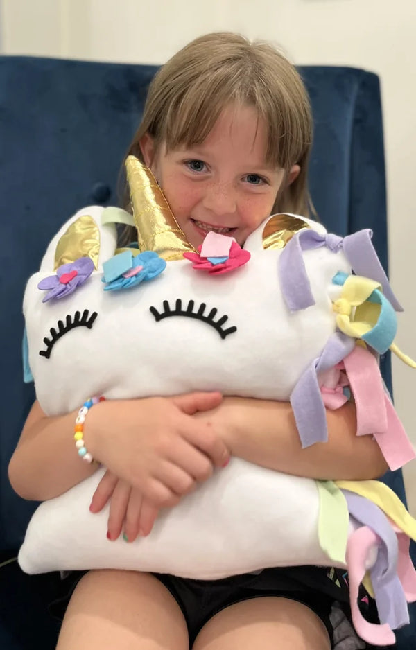 Girl on a blue chair squeezing the finished unicorn pillow she made