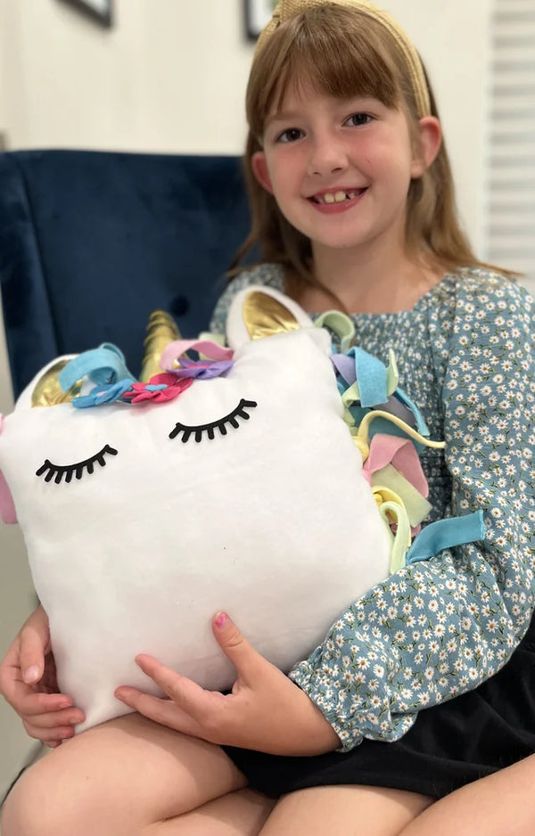 Smiling girl holding up the finished unicorn pillow she made from the kit