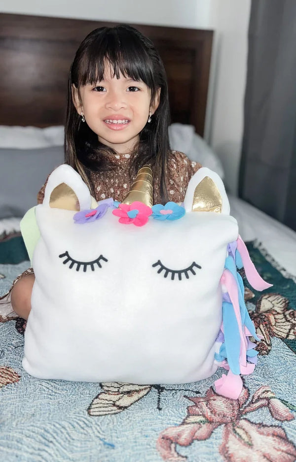 Girl on a bed peeking out from behind her finished unicorn pillow