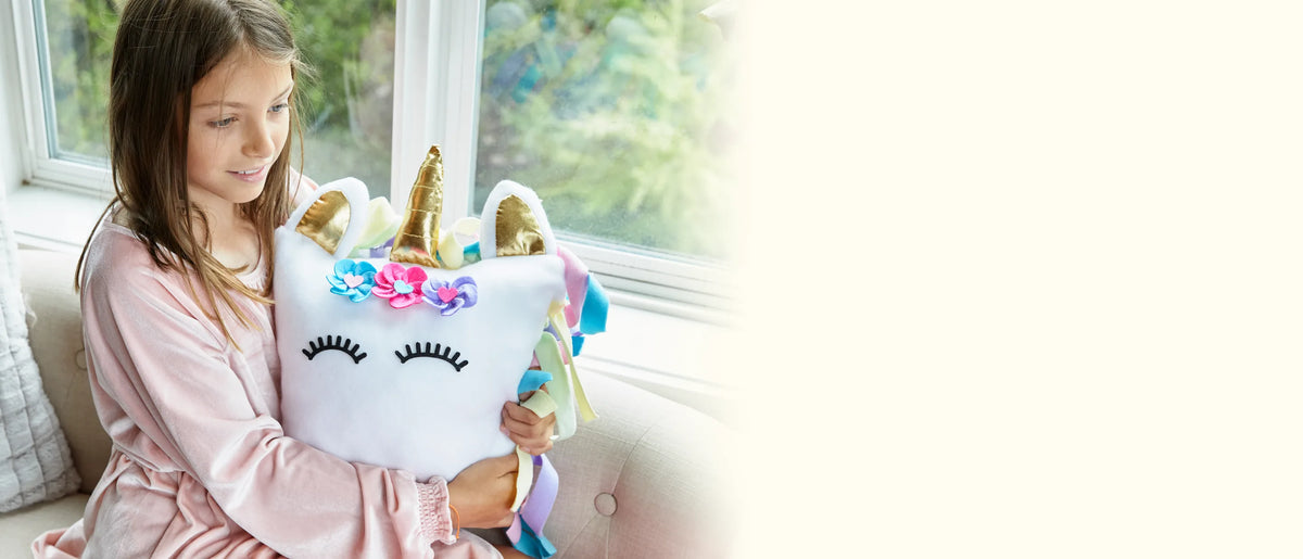 Girl on a window seat hugging the finished white unicorn pillow she made
