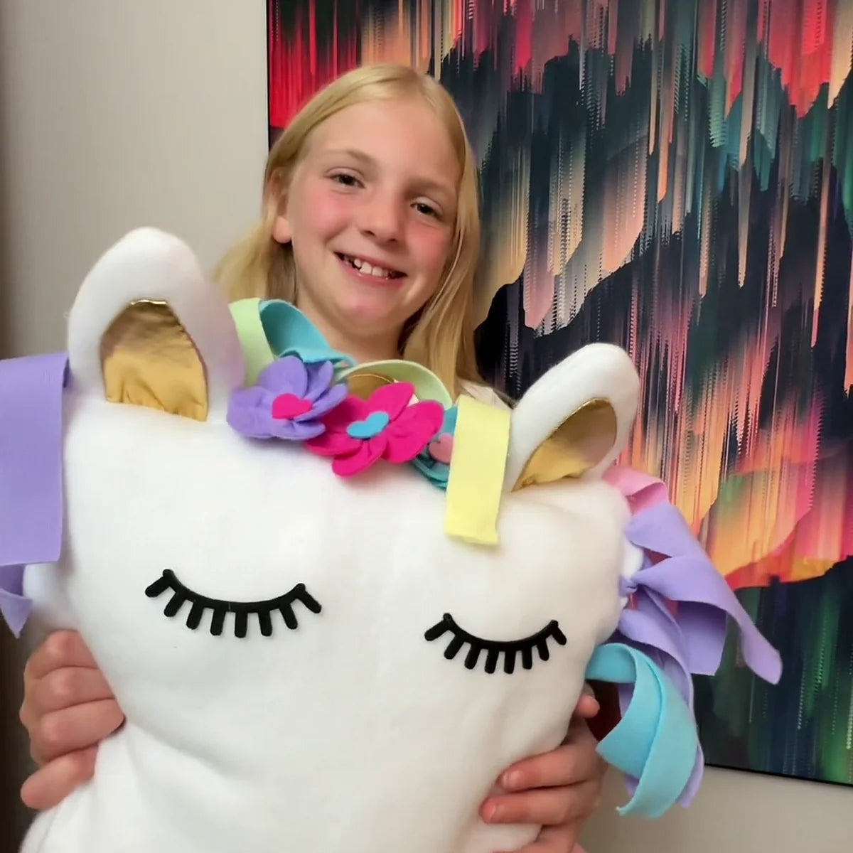 Girl smiling over the finished unicorn pillow she tied, stuffed and decorated