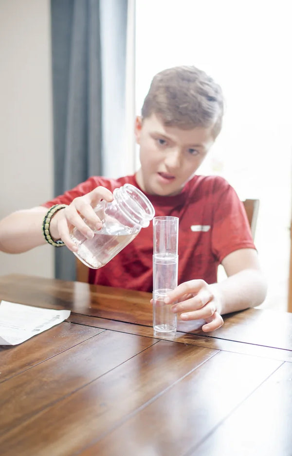 Boy in a red T-shirt pouring water from a jar into the water filter tower at the table