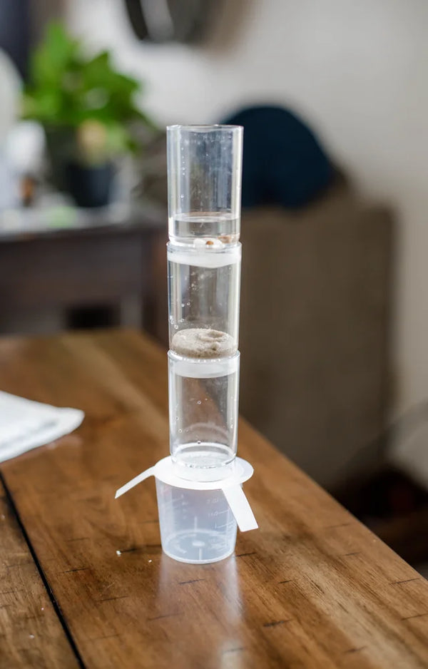 The finished clear water filter tower standing on its support card over a cup on a wooden table