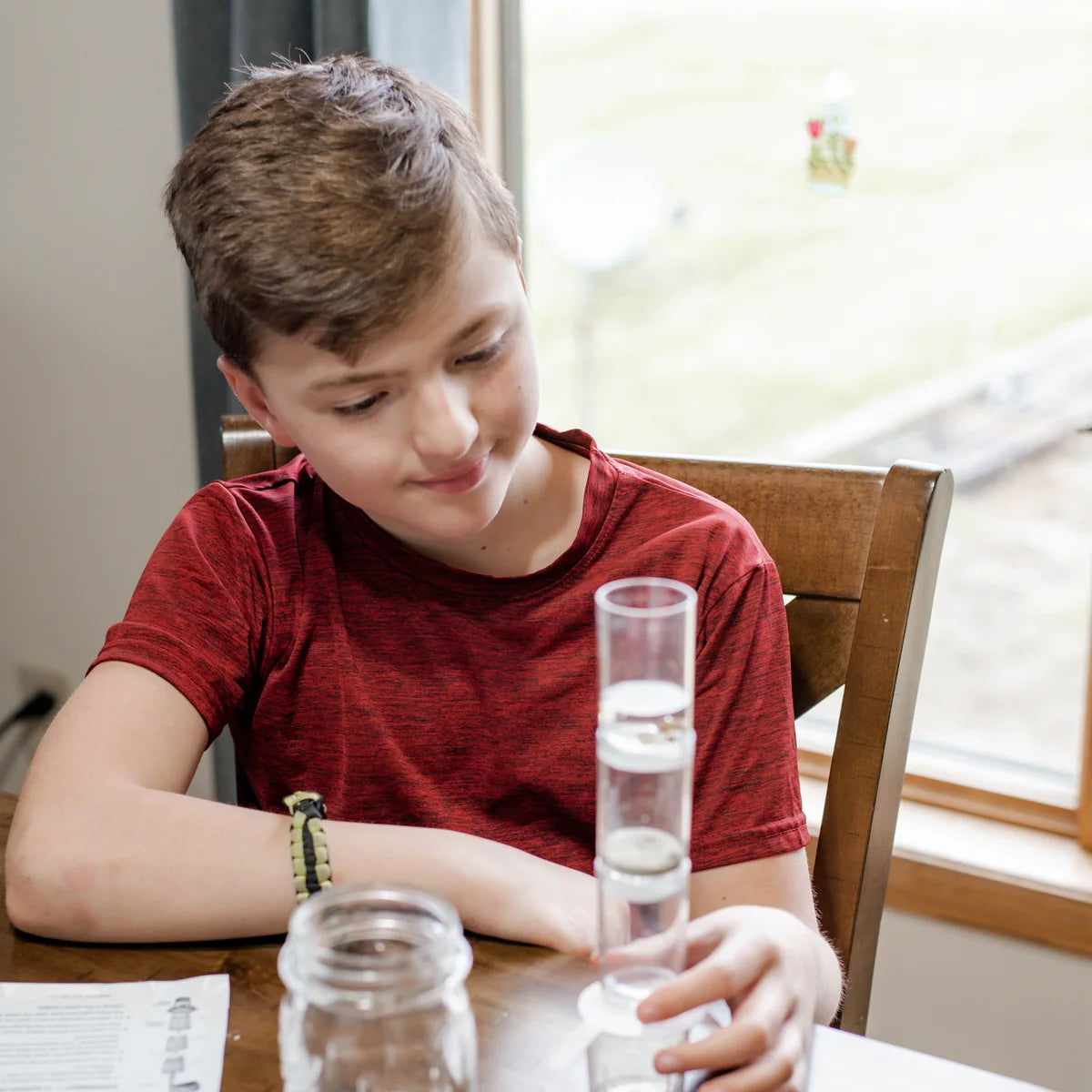 Boy smiling at his clear water filter tower on the kitchen table, with a jar of water beside it