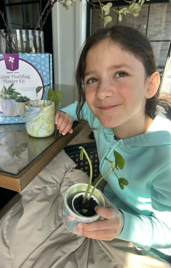 Smiling girl holding her marbled pot with a small potted cutting, the second pot and box behind her